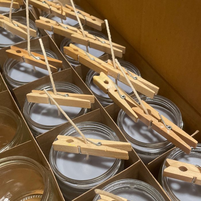 Candles setting in clear glass jars, wicks held straight with clothespins